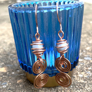 Aquamarine bead encased in cooper wire with swirl design create these dangle earrings.