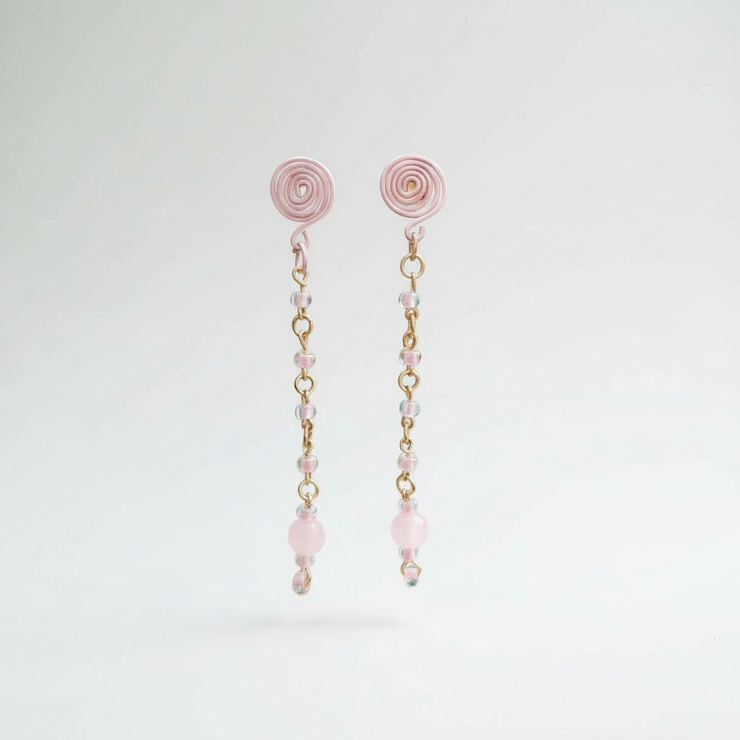 Pair of pink spiral earrings with gold chain and beads on a light gray background
