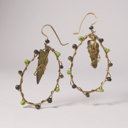 Pair of gold hoop earrings with green glass and green beads on a light gray background