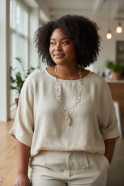 Black woman with natural hair in beige clothes wearing necklace.