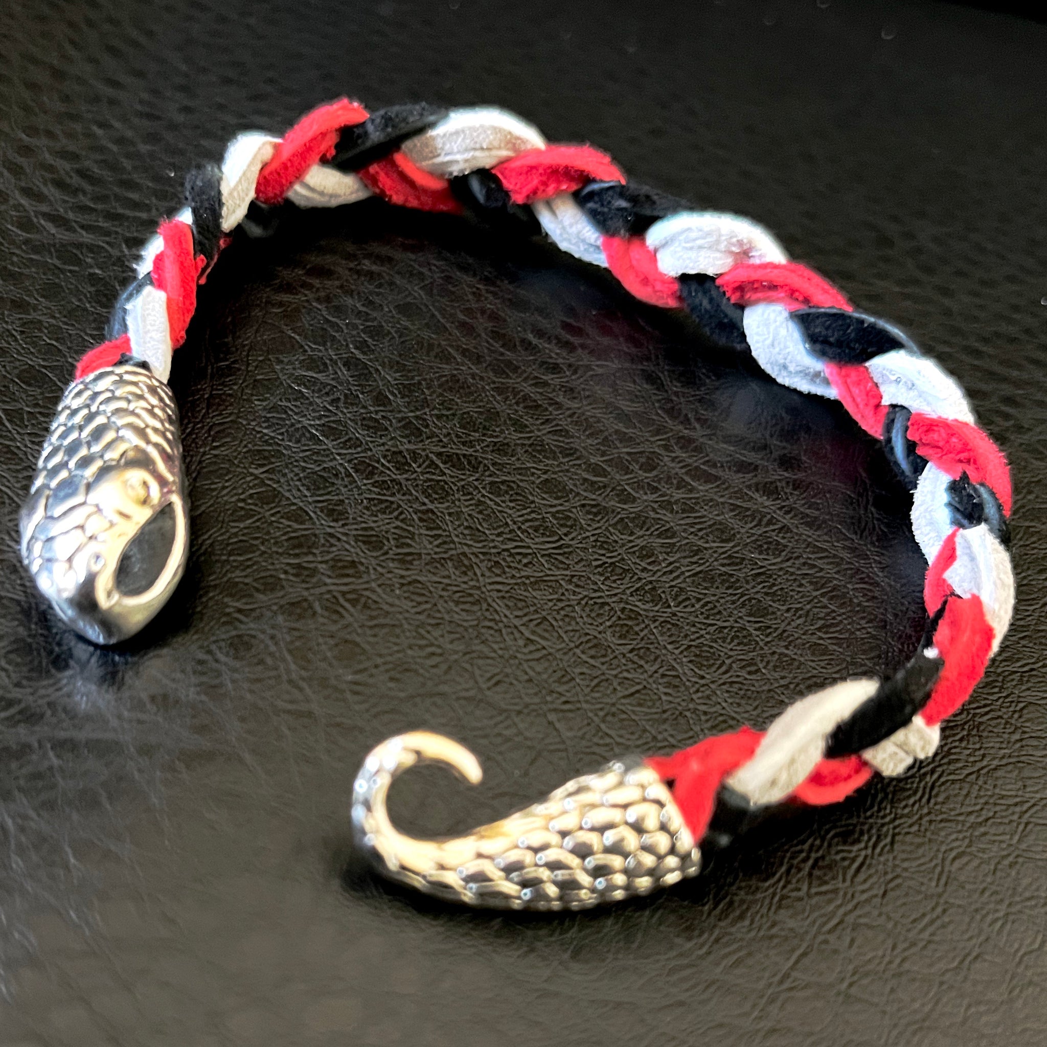 Bracelet made with grey, black, and red braided suede cord with silver tone snake clasp. 