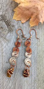 Circular patterns of alternating rose gold and antique wire create dangle earrings.  Recycled brown glass from a beer bottle hang from the bottom with a jump ring. 