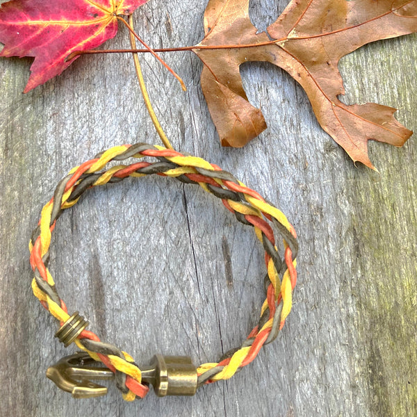 Braided suede cord in the colors of army green, mustard yellow, and rust orange with brass anchor clasp has sliding stopper. 